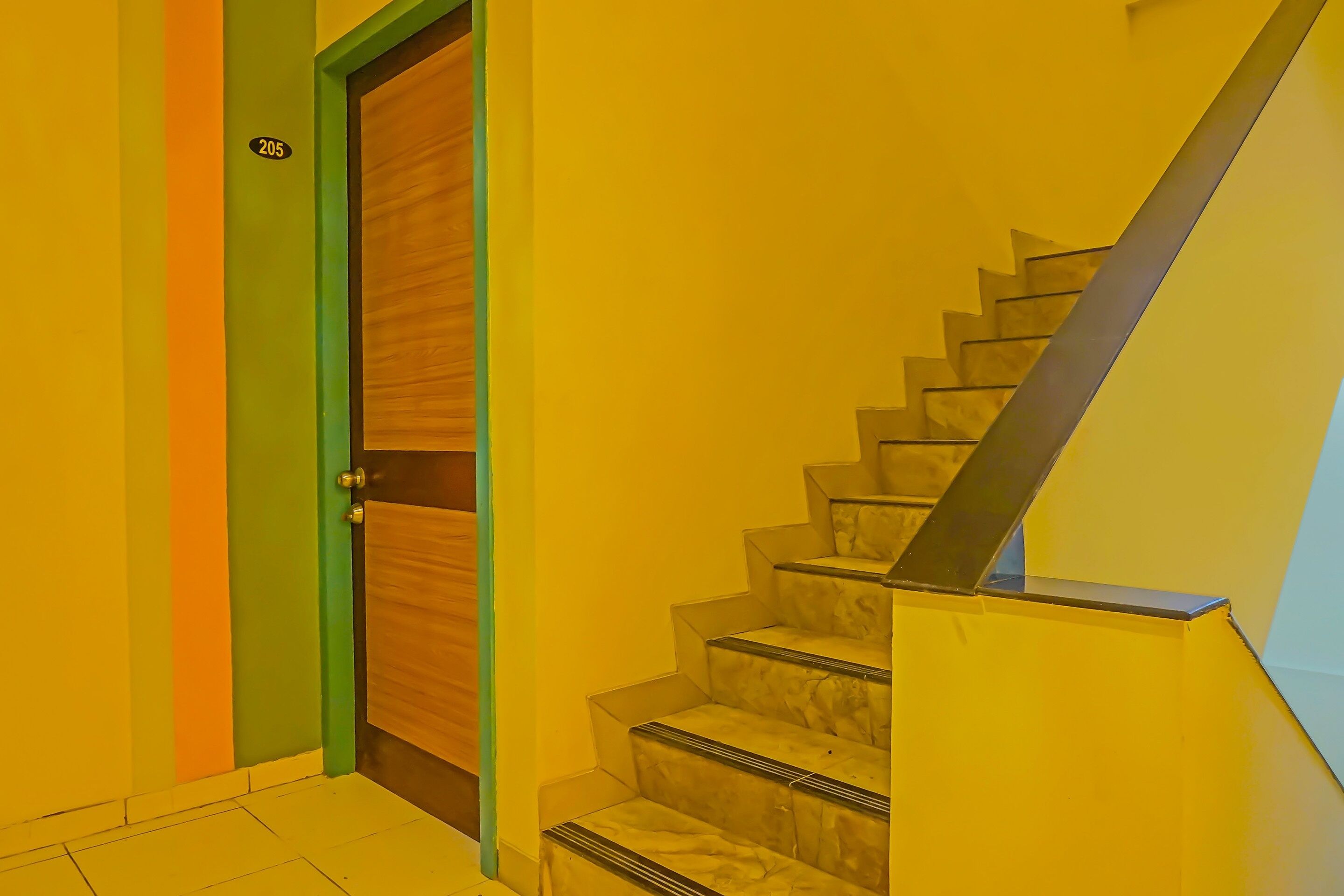 A staircase with marble steps and a metal handrail, leading to a room with a wooden door and a green frame.