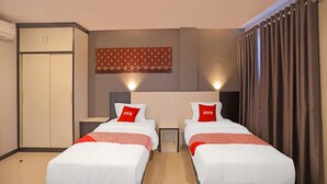 Ett hotellrum med två sängar, en garderob, ett litet bord och en väggbonad med mönster.