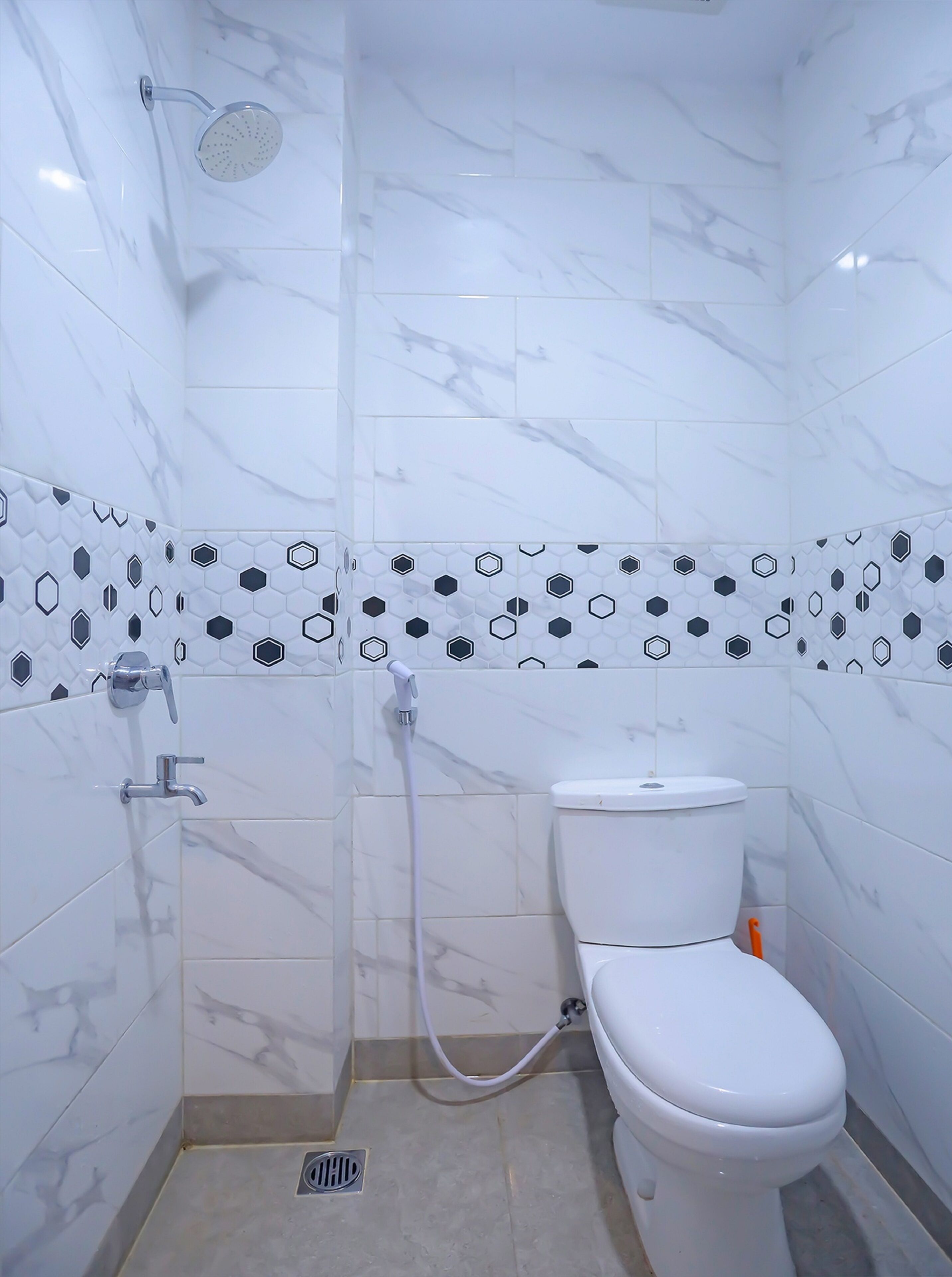 Une salle de bain avec des carreaux de marbre blanc, des toilettes, une douche avec un pommeau de douche amovible et un porte-rouleau de papier toilette.