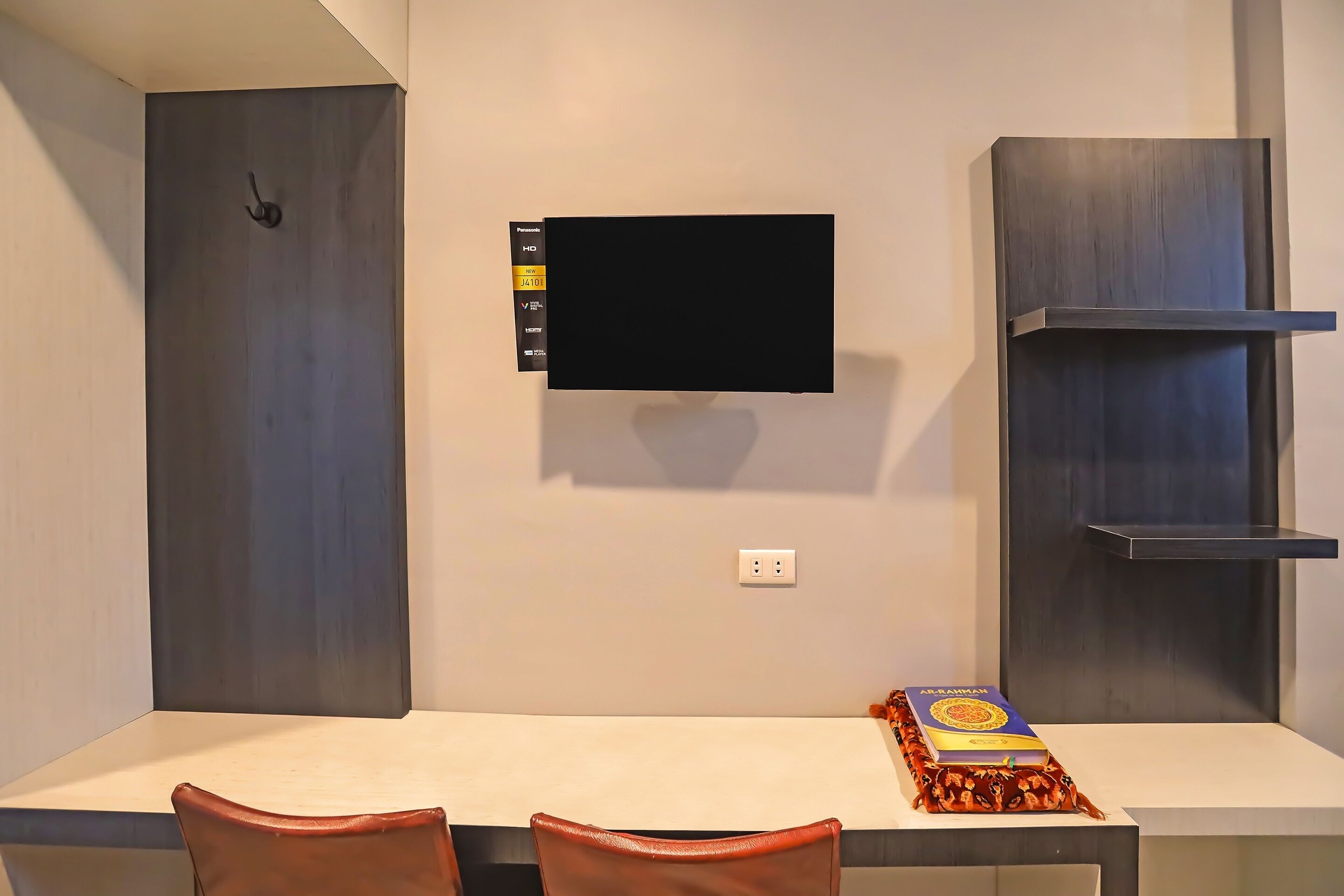 A modern room with a flat-screen TV mounted on the wall, a white table, and two brown chairs.