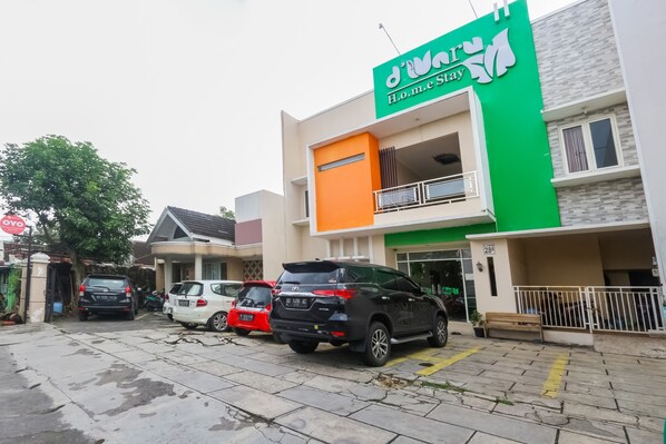 A modern two-story building with a green and white facade, a balcony, and a parking area with several cars. - OYO 90193 D'waru Homestay Syariah (Surakarta)