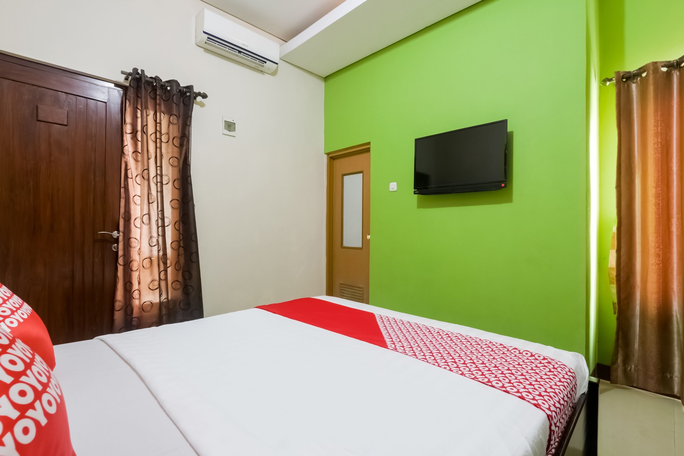 A room with a bed, a television on the wall, and a door.