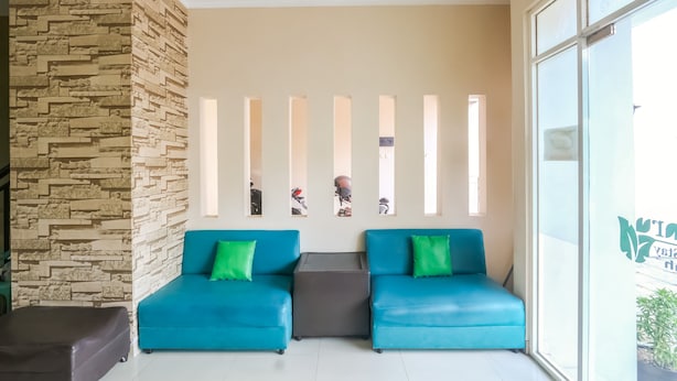 A reception area with a stone wall, two blue sofas with green cushions, a small grey table, and a large window with a view.