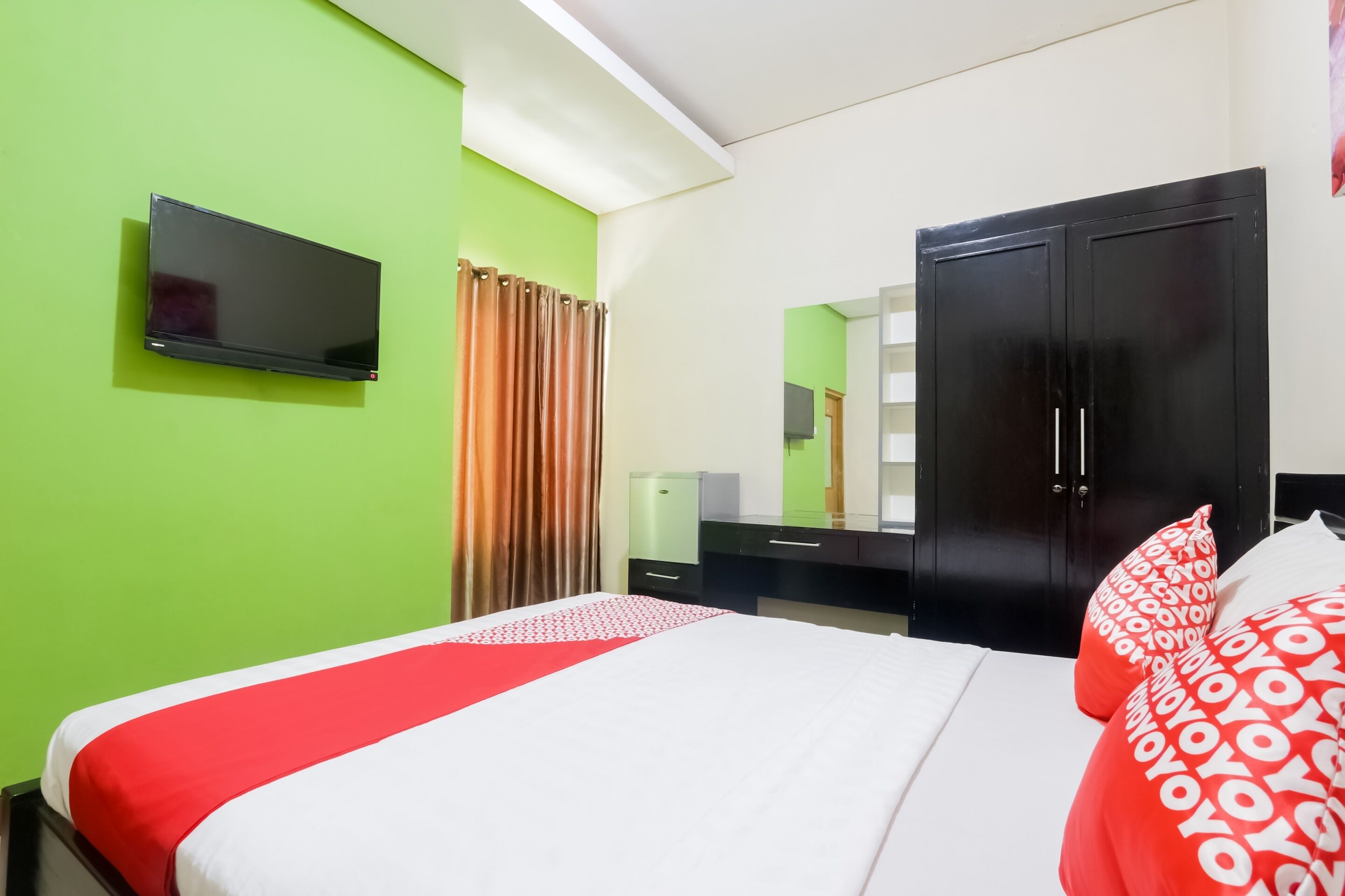 A hotel room with a bed, a flat-screen TV, a wardrobe, and a mirror.