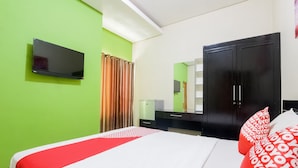 A hotel room with a bed, a flat-screen TV, a wardrobe, and a mirror.