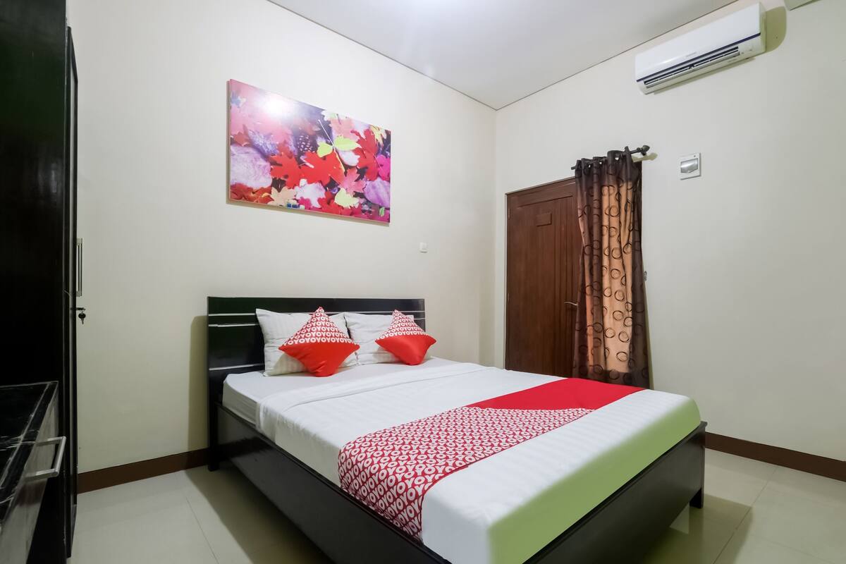A neatly arranged bedroom with a bed, a wall-mounted air conditioner, and a door with patterned curtains.