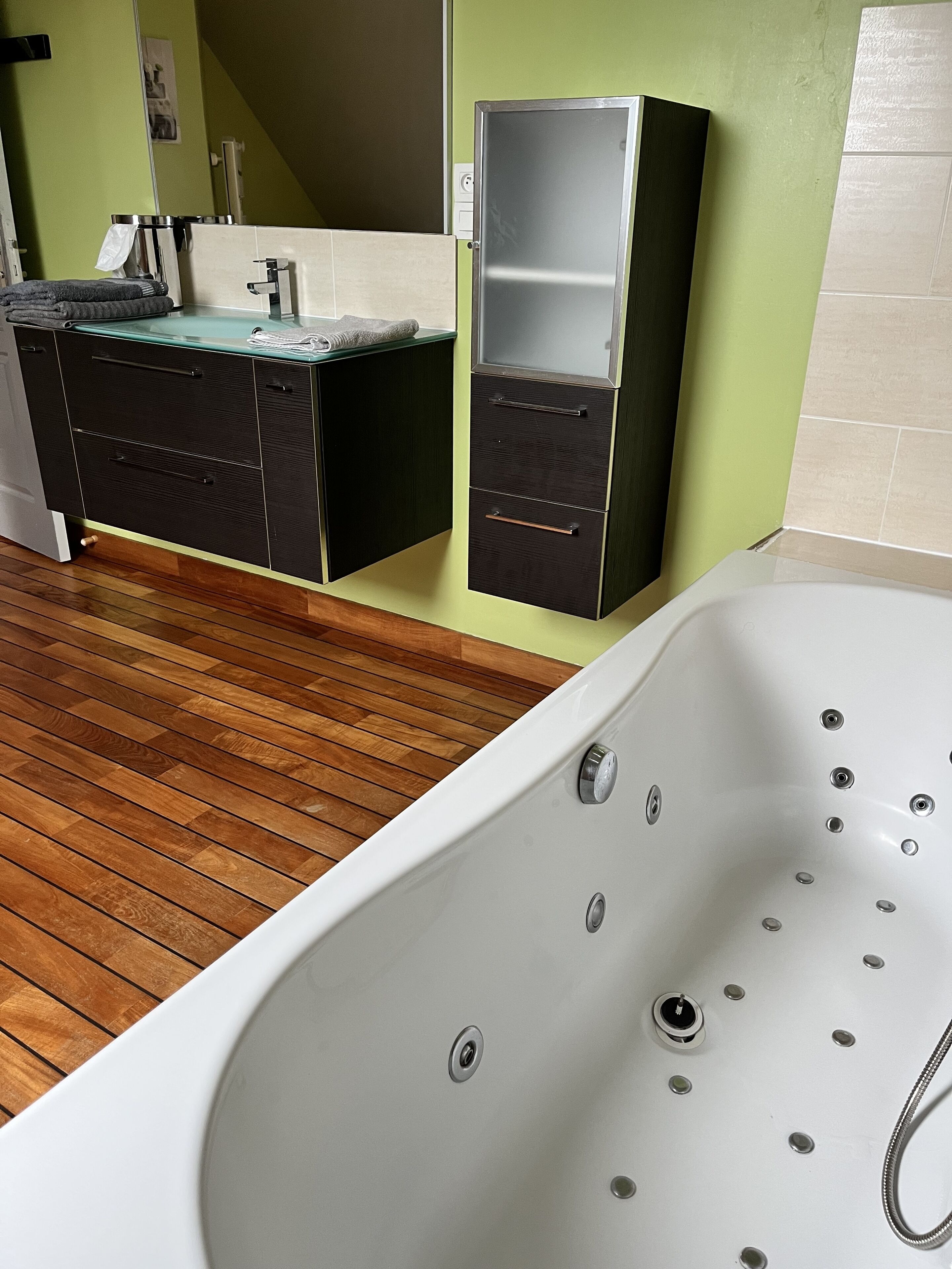 Un baño moderno con suelo de madera, una bañera blanca y un tocador empotrado con espejo.