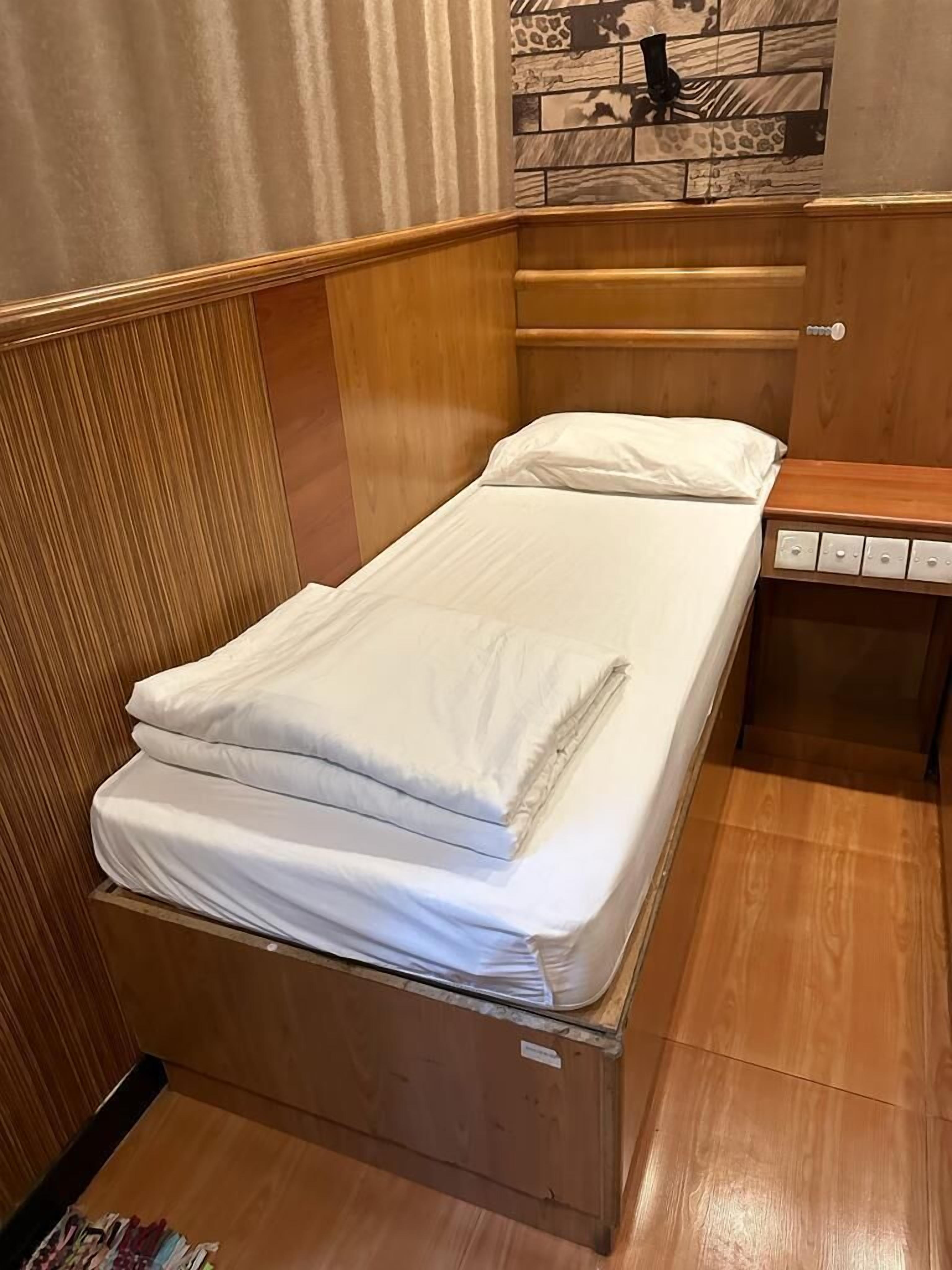 A single bed with white linens in a room with wooden paneling and a tiled wall decoration.