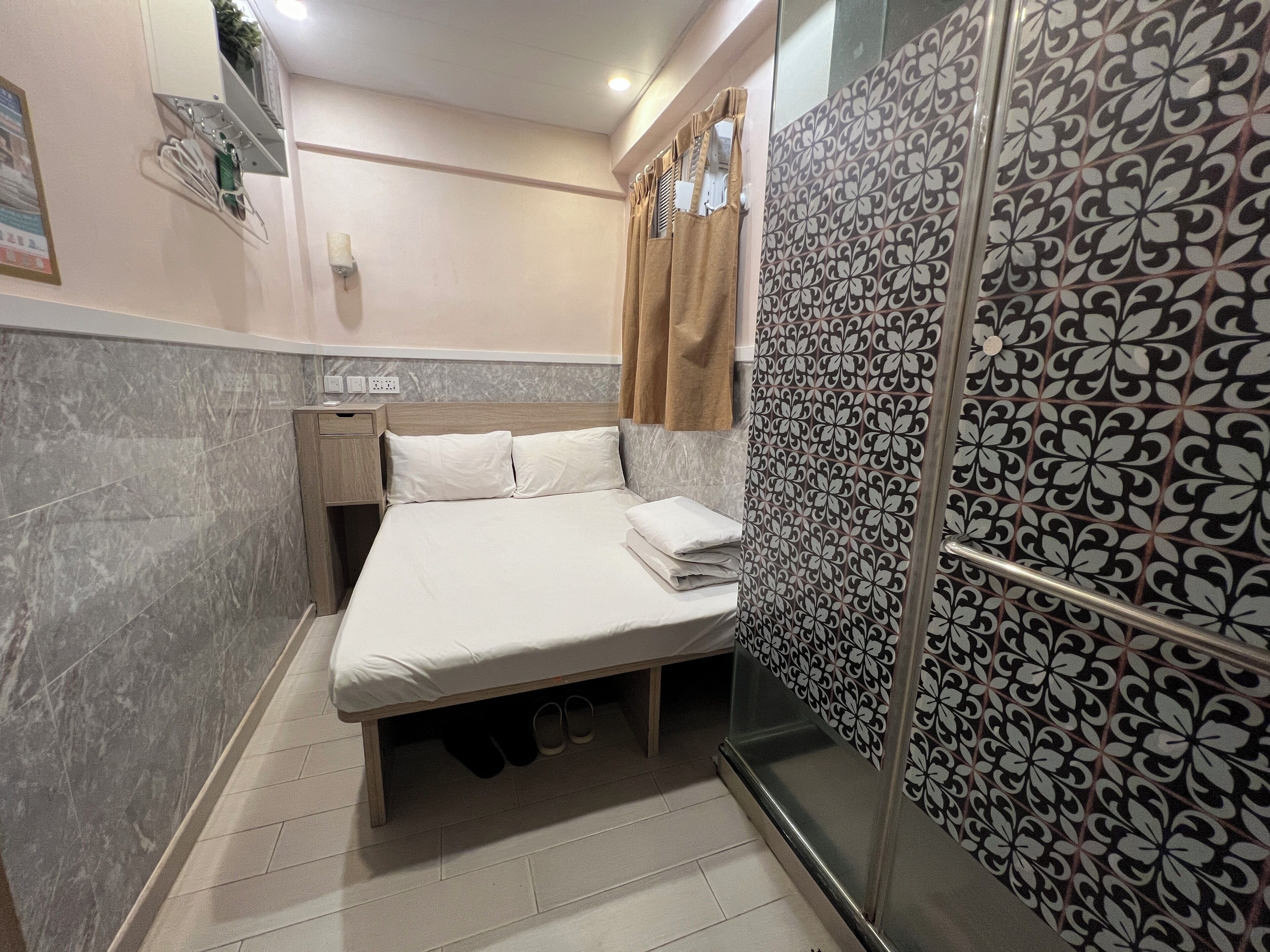 A hotel room with a bed, a nightstand, a shower area, and a patterned wall.