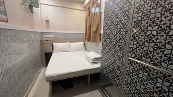 A hotel room with a bed, a nightstand, a shower area, and a patterned wall.