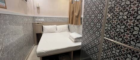 A hotel room with a bed, a nightstand, a shower area, and a patterned wall.