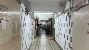Ein Flur mit Fliesenboden, Türen an beiden Seiten sowie sichtbaren Rohren und Lüftungsanlagen an der Decke.