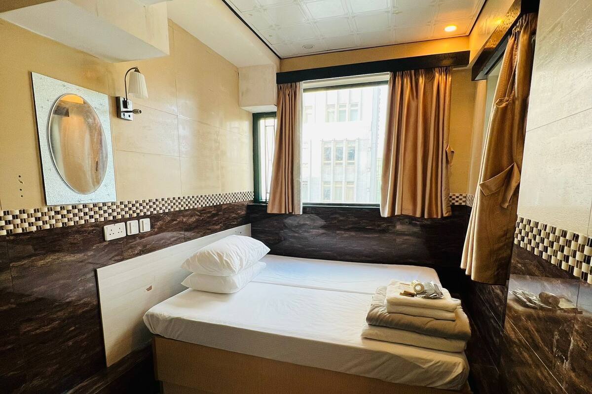 Une chambre d’hôtel avec un lit, un grand miroir, une fenêtre avec des rideaux et un pare-feu en carreaux.