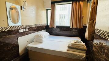 A hotel room with a bed, a large mirror, a window with curtains, and a tiled backsplash.