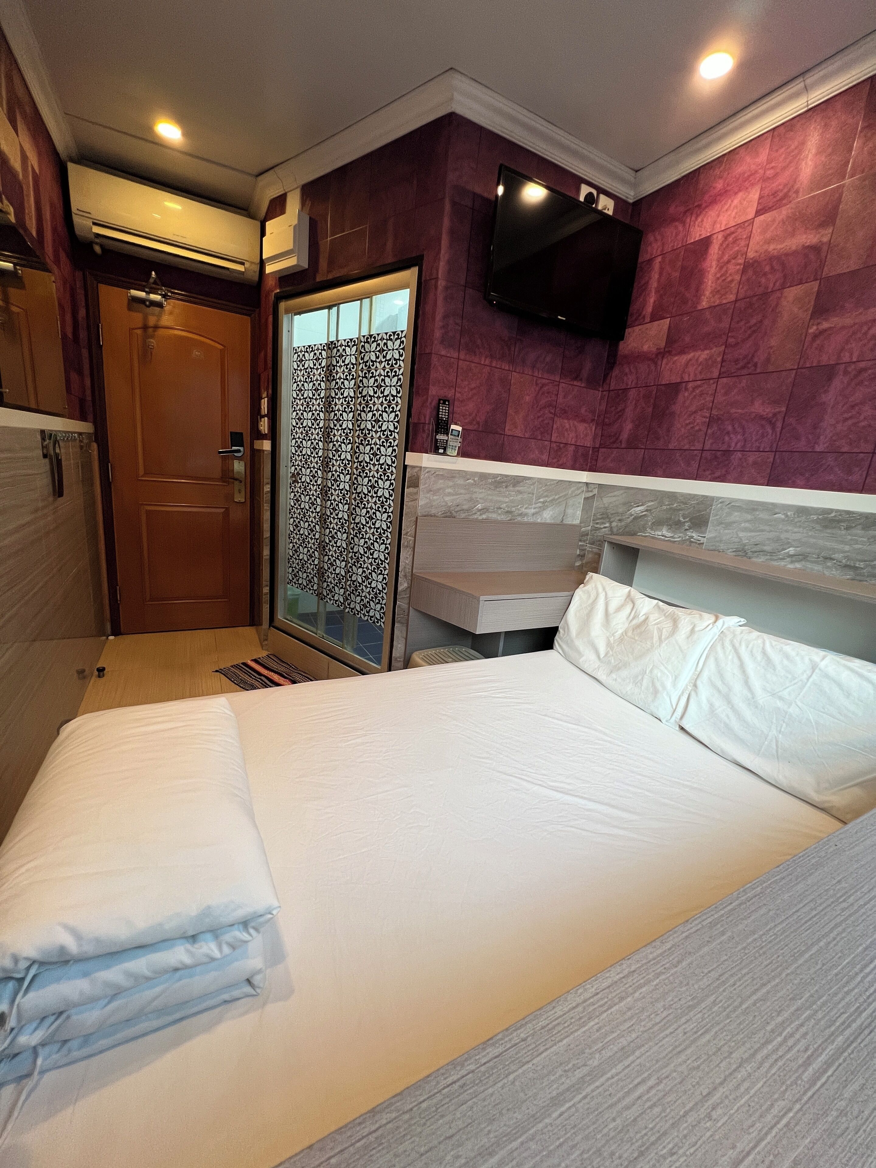 A hotel room with a bed, a shower, a vanity with a mirror, and a mounted TV.