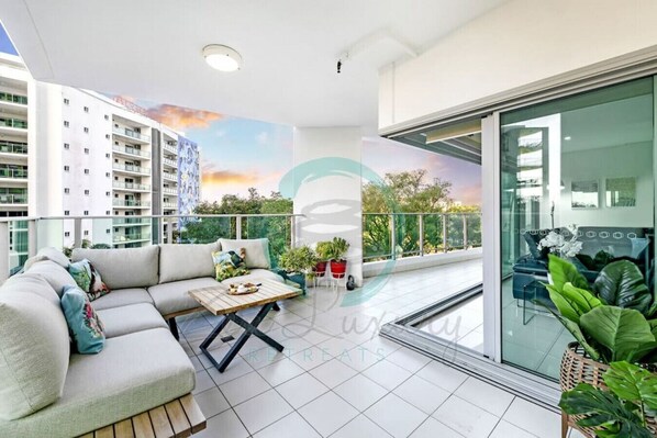 A modern balcony with a sofa, a small table, and potted plants. - ZEN TREE BLOSSOM - 3BR Luxury Apartment (Darwin)