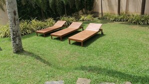 Tres sillones de madera dispuestos sobre un césped cuidado, con una variedad de plantas tropicales al fondo.