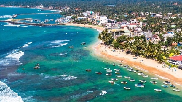 Vista aérea de un pueblo costero con playa, barcos y edificios.