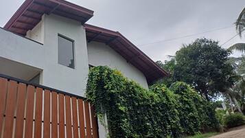 A modern house with a white exterior, a wooden fence, and lush greenery.
