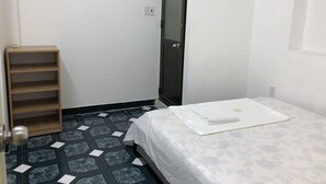 Een kleine, schone kamer met een bed, een houten plank en een deur.