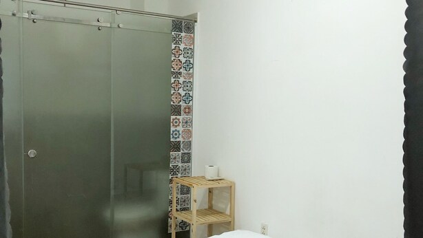 Een hotelkamer met een bed, een houten plank, een douche en een wandairconditioner.