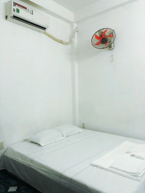 A small, clean room with a bed, a wall-mounted air conditioner, and a ceiling fan.
