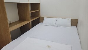 Een klein, net opgemaakt bed met witte lakens en kussens, houten planken en een witte muur.