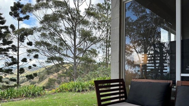 Ein moderner Außenbereich mit einer Bank und einer Couch, mit Blick auf einen angelegten Garten und Hügel.