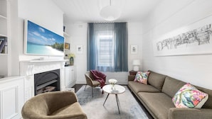 Un salon avec une cheminée, un canapé, un fauteuil, une petite table ronde et un tableau accroché au mur.