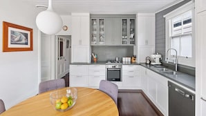 Une cuisine moderne avec des meubles blancs, une table à manger en bois et un saladier rempli de fruits.