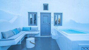 Une pièce moderne et minimaliste, dotée d’un coin salon intégré, d’une baignoire et d’une petite table ronde.