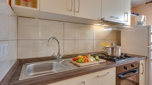 A modern kitchen with a stainless steel sink, a cutting board with vegetables, a stove, and a coffee maker.
