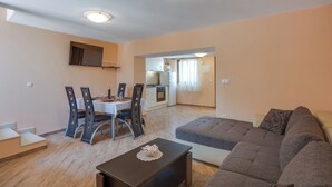 A modern living room with a sofa, dining table, chairs, and a kitchen in the background.