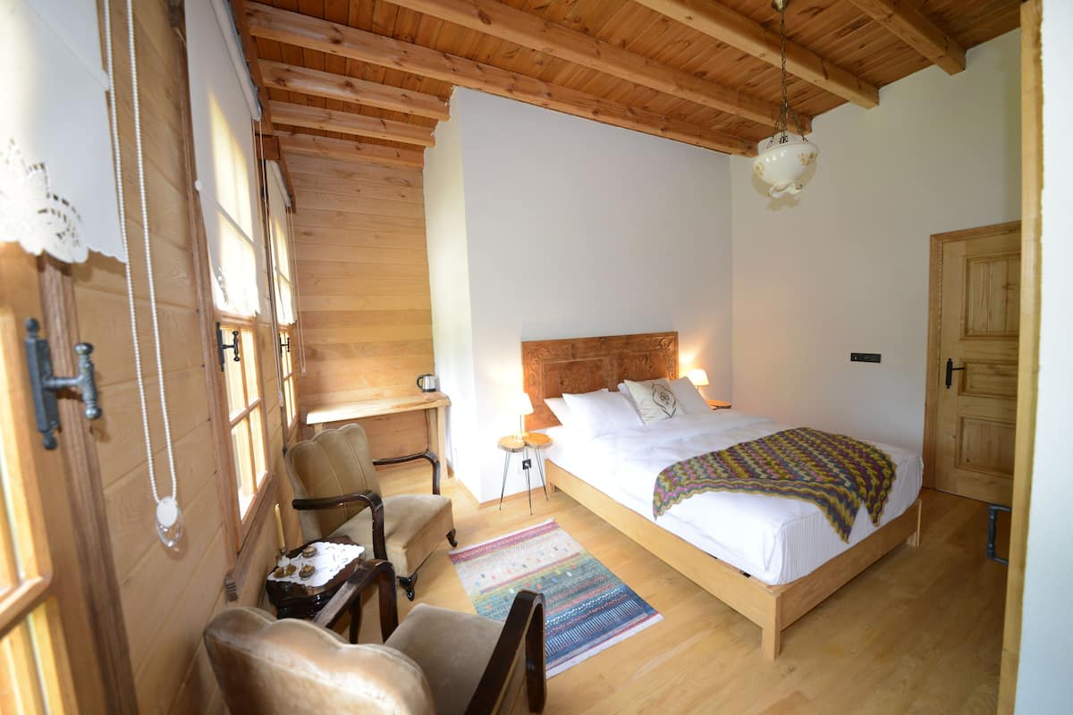 Un dormitorio con paneles de madera, una cama, una silla, una mesita y una mesita de noche.
