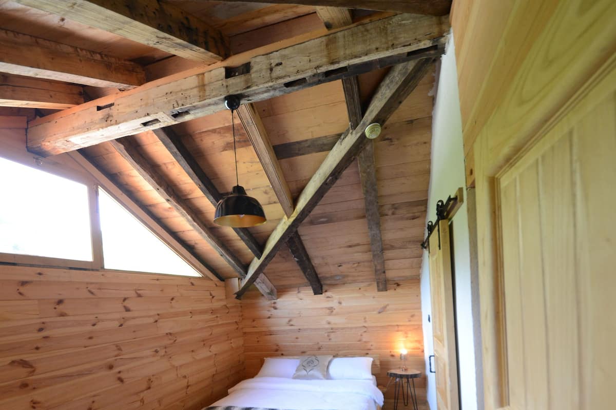 Una habitación de cabaña de madera con una cama, una mesita y una ventana.