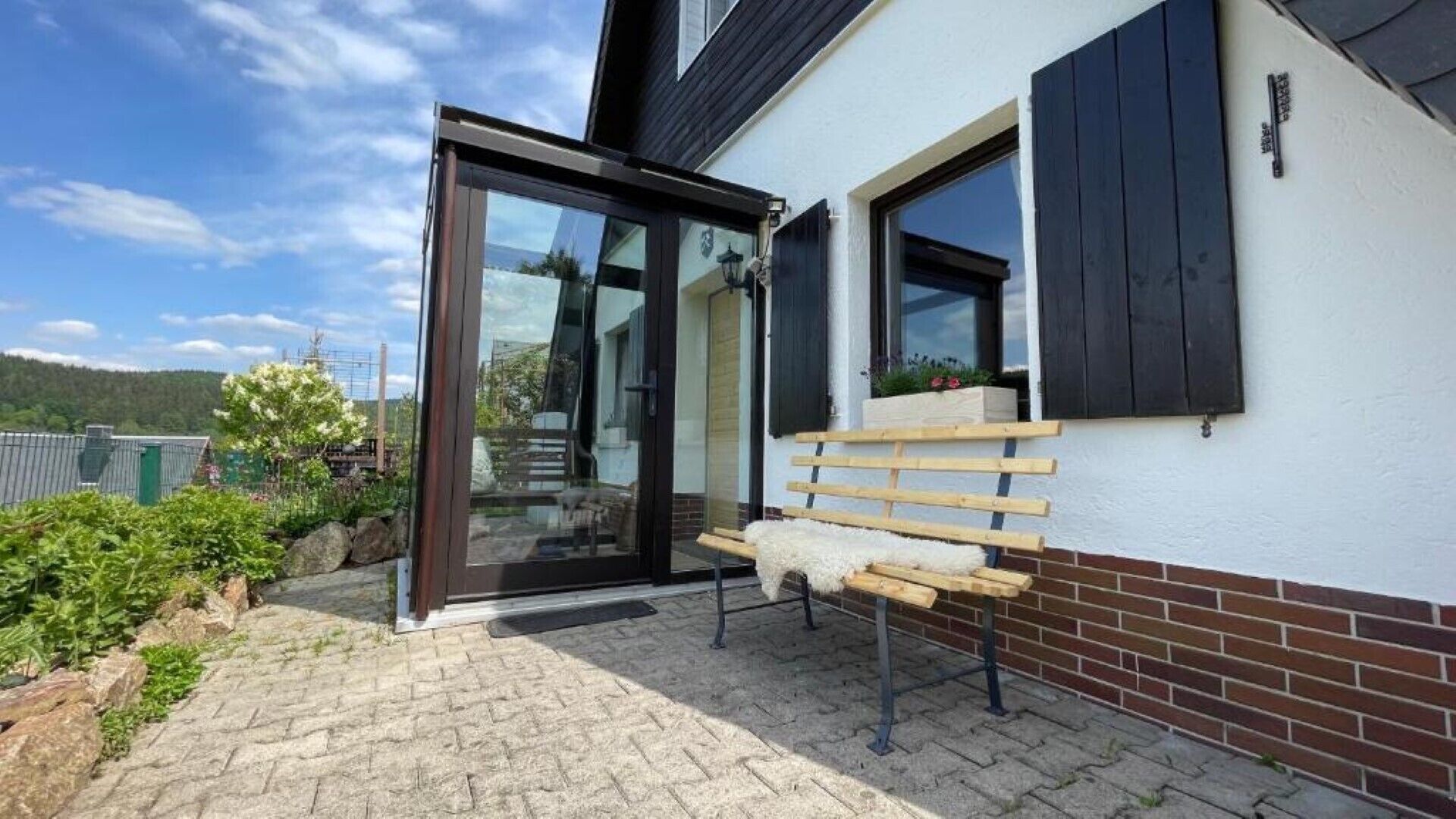 A modern house with a glass door entrance, a wooden bench outside, and a brick pathway.