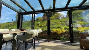 Une véranda avec un toit en verre, une table à manger avec des chaises et un mur en pierre.