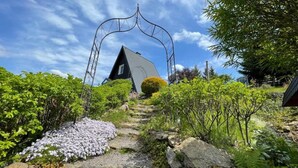 Une maison dotée d’un toit triangulaire original, entourée d’une végétation luxuriante et sous un ciel dégagé.