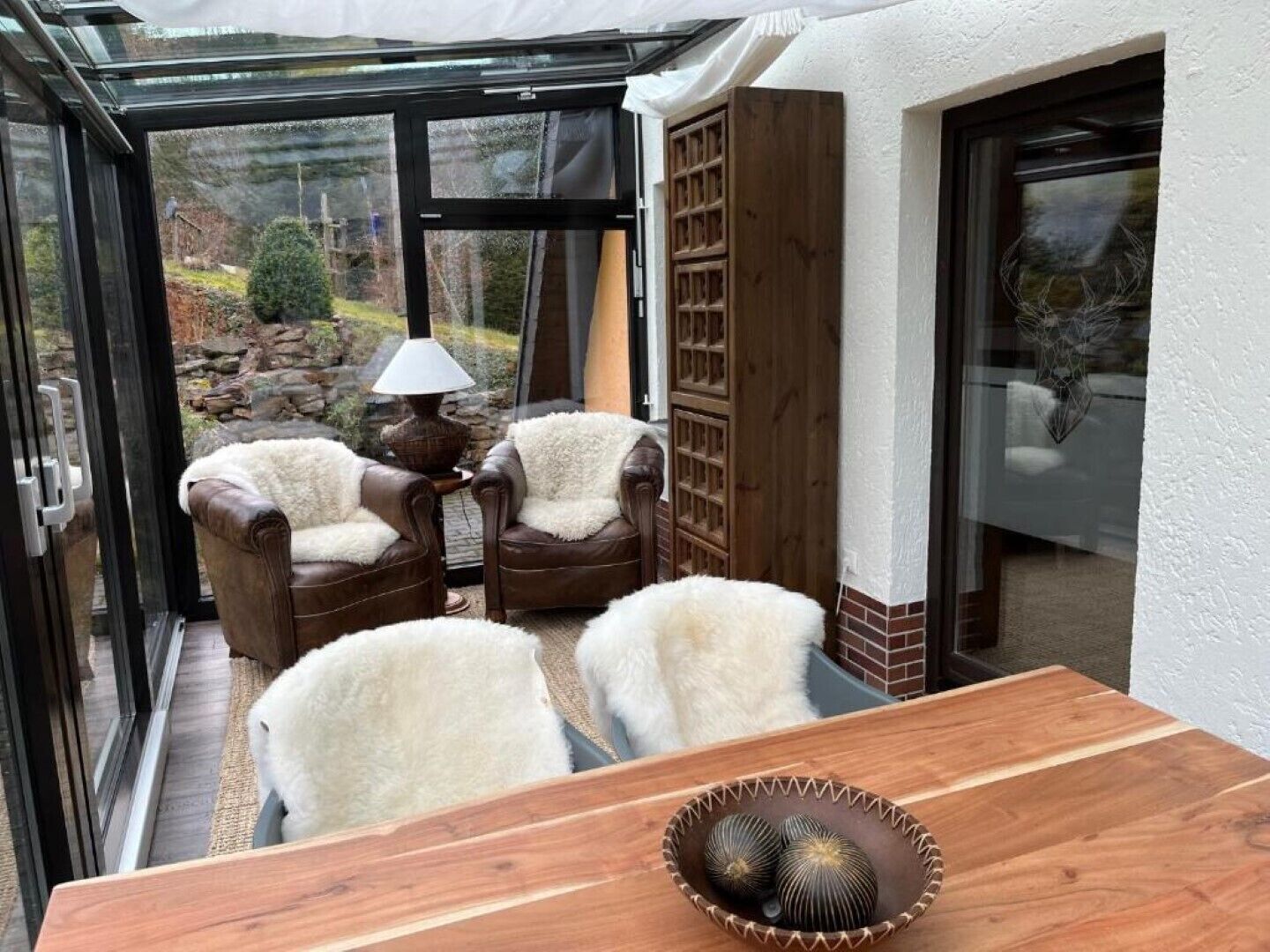 A glass-enclosed patio with two leather armchairs, a wooden table, and a decorative bowl.