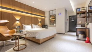 A modern hotel room with a large bed, a sitting area with a chair and table, a mirror, and a small kitchenette. - NOMAD HOTEL (Gimhae)