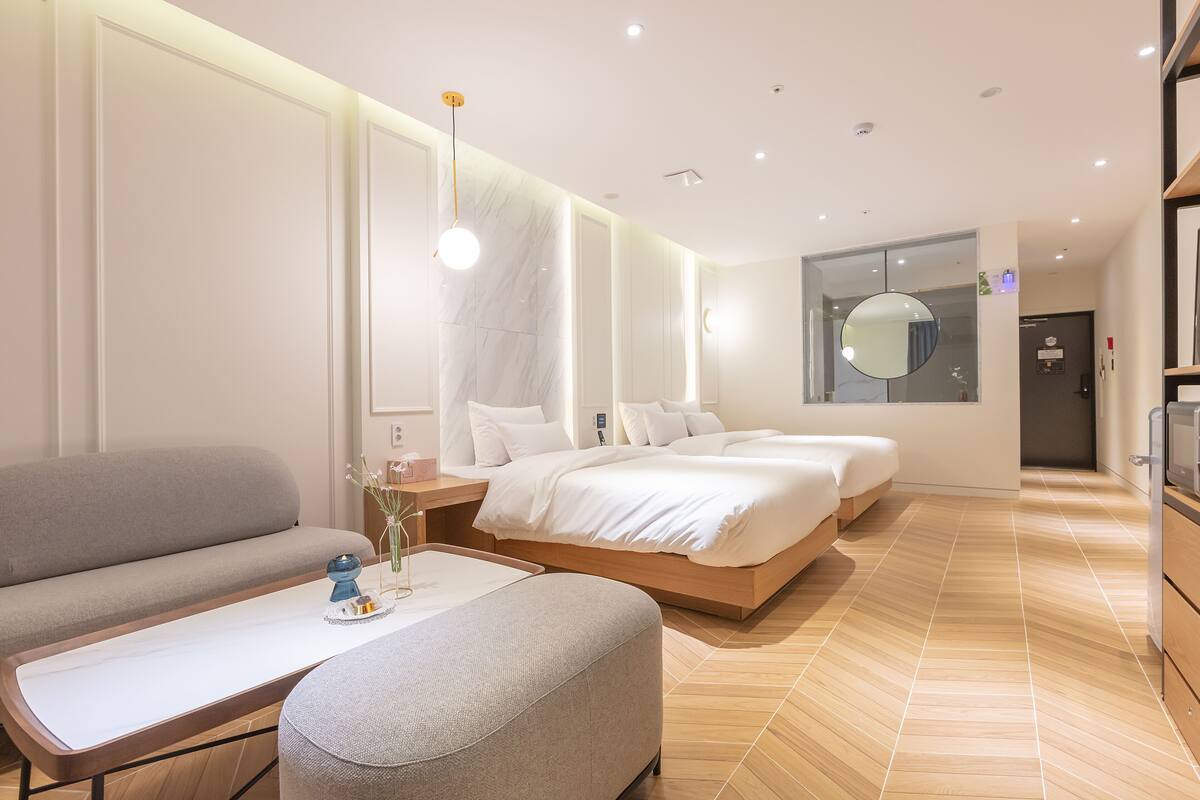A modern hotel room with a sofa, a bed, a bedside table, and a mirror.