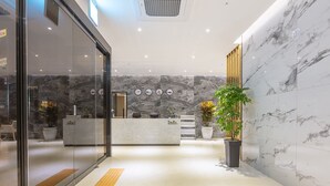 A reception area with a marble wall, a reception desk, and a potted plant. - NOMAD HOTEL (Gimhae)