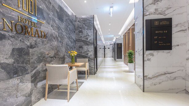 A hotel lobby with a marble wall, a reception desk, and a sign indicating the front and day & day cafe. - NOMAD HOTEL (Gimhae)