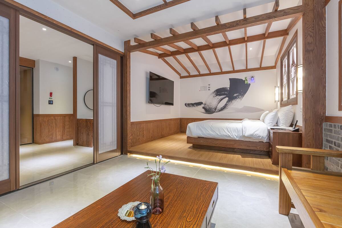 A modern hotel room with a wooden ceiling, a bed, a bedside table, and a wall-mounted TV.