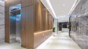 A modern elevator with a wooden panel design, a reception desk with a potted plant, and a marble wall. - NOMAD HOTEL (Gimhae)