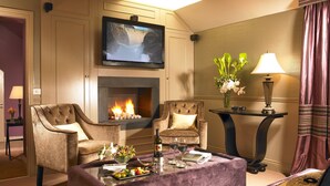 A living room with a fireplace, two armchairs, a coffee table with fruit and wine glasses, and a television mounted above the fireplace. - Old Bank House Kinsale (Kinsale)