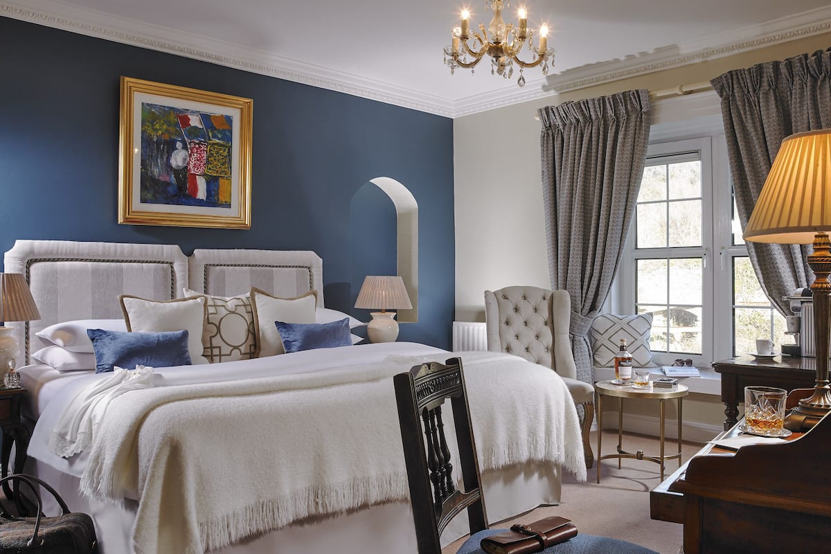 A well-appointed bedroom with a large bed, a sitting area with a piano, and a view of the outdoors through a window.