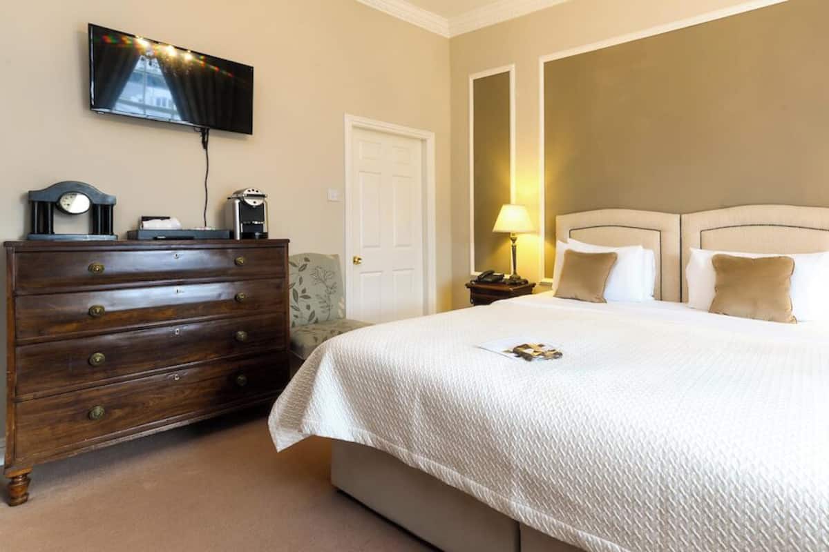 A hotel room with a large bed, a dresser, a television mounted on the wall, and two bedside lamps.