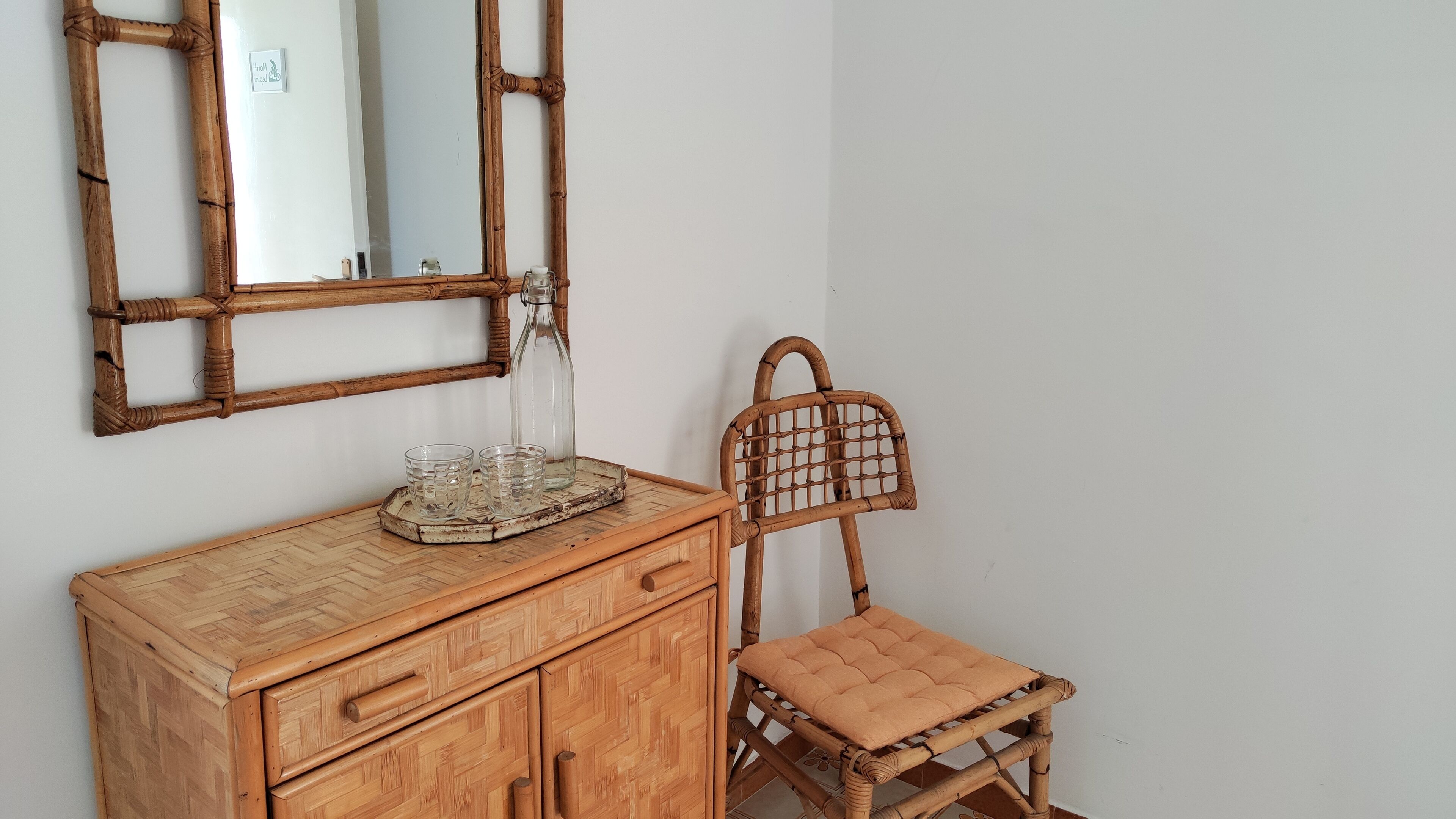 A wooden dresser with drawers and a mirror above it. There is a wicker chair with a cushion next to the dresser.