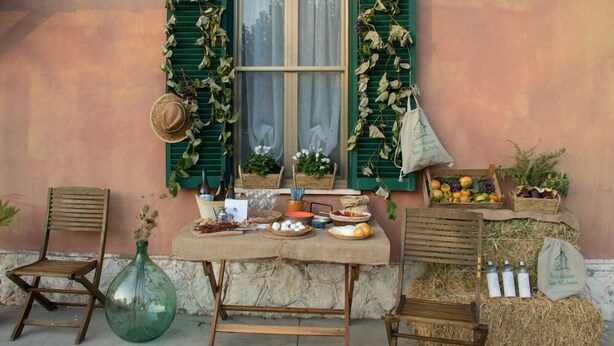 A rustic outdoor setting with a table set for a meal, a green window with shutters, and various food items and decorations. - Eco House San Michele (Latina)